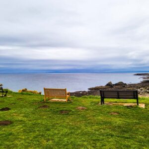 Park benches viewed from behind at the top of a clif with a view of the sea.